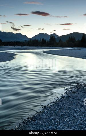 L'Isar in Werdenfelser Land, circondato dalle Alpi Bavaresi. La luce della sera si riflette nell'acqua, che scorre attraverso il fondo di ghiaia poco profondo con piccole isole. Foto Stock