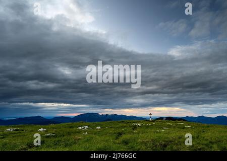 Un piccolo sentiero conduce alla croce sommitale del Vorderskopf nel Karwendel, in un'atmosfera densa e nuvolosa. Foto Stock