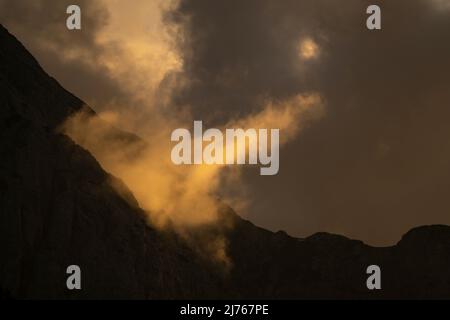 Luce notturna con una speciale atmosfera da nuvola sul Wetterstein sopra Mittenwald. In alcune immagini di questa serie ancora un'aquila d'oro vola in piccolo vicino alla croce di cima Foto Stock