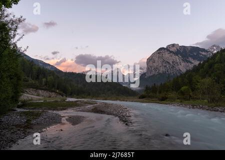 Nuvole leggermente colorate e l'acqua che scorre al Rissbach nel Parco Naturale del Karwendel, poco prima del Großer Ahornboden. In primo piano il torrente, sullo sfondo montagna e luce del tramonto. Foto Stock
