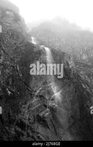 Piccola cascata a Karwendel nelle Alpi nella nebbia. La cascata si trova vicino al Gradai Hochleger nel parco naturale e cade su una parete di roccia impressionante. Foto Stock