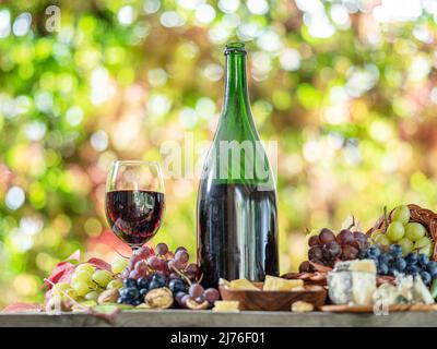 Uva, bottiglia di vino e formaggi diversi su tavola di legno di campagna e sfocato sfondo colorato autunno. Varietà di prodotti come il simbolo di autu Foto Stock