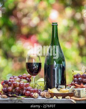 Uva, bottiglia di vino e formaggi diversi su tavola di legno di campagna e sfocato sfondo colorato autunno. Varietà di prodotti come il simbolo di autu Foto Stock