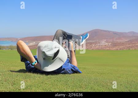 Un uomo sdraiato in erba, si rilassa guardando il suo cellulare. Foto Stock