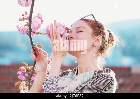 Giovane donna rossa allegra in poncho odore di ciliegia fiore nel parco Foto Stock