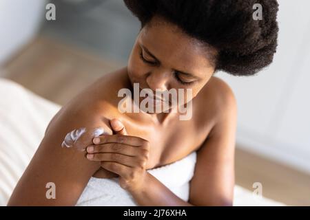 Donna di metà adulta afroamericana che applica moisturizer sul braccio a casa Foto Stock