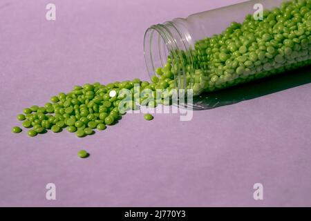 Splendidi granuli di cera verde con estratto di aloe per la depilazione vengono versati su uno sfondo viola chiaro, da un vaso trasparente. Epilazione, depilazione Foto Stock