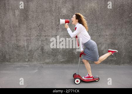 Felice donna d'affari che guida scooter. Ritratto all'aperto di una giovane donna che gridava attraverso l'altoparlante. Torna al concetto di idea di lavoro, di avvio e di business Foto Stock