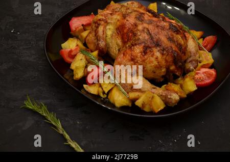 Pollo arrosto o tacchino alla griglia per Natale o Ringraziamento in salsa con patate verdure e rosmarino in un piatto di servizio nero. Backgroun scuro Foto Stock