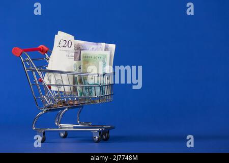 Carrello mini con banconote in contanti nel carrello su sfondo blu Foto Stock