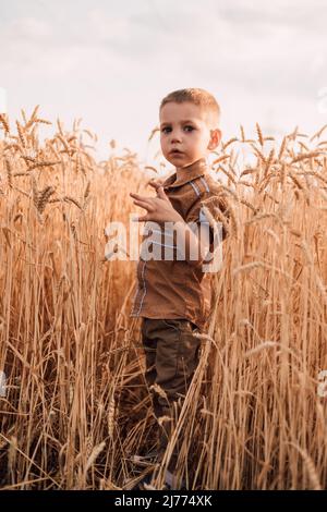 Un bambino piccolo si trova in un campo con il grano contro il cielo Foto Stock