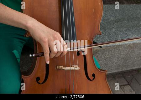 Dettaglio di un uomo che suona il violoncello di legno strofinando le corde con l'arco per ottenere le note di un pezzo di musica classica. Foto Stock