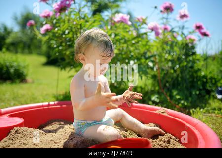 Adorabile ragazzo toddler che gioca in un sandbox durante la giornata estiva calda e soleggiata. Bambini che esplorano la natura. Tempo libero attivo per famiglie con bambini piccoli. Foto Stock