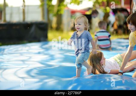 Carino ragazzo piccolo e le sue due sorelle che rimbalzano su un enorme cuscino di salto riempito d'acqua. Ragazzo che salta su e giù sul pad rimbalzante. Attività per famiglie Foto Stock