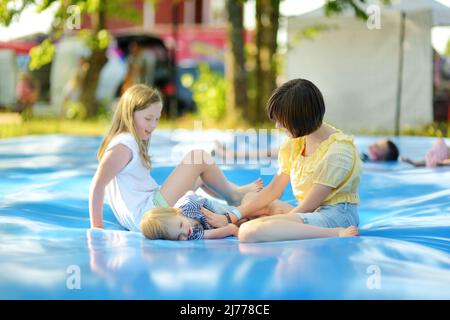 Carino ragazzo piccolo e le sue due sorelle che rimbalzano su un enorme cuscino di salto riempito d'acqua. Ragazzo che salta su e giù sul pad rimbalzante. Attività per famiglie Foto Stock