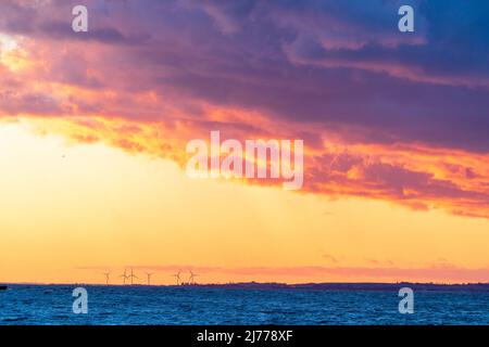 Sei turbine eoliche sull'isola di Sheppey viste da Herne Bay attraverso l'estuario del Thomas. Orizzonte basso con il cielo drammatico del tramonto e la nuvola spessa più in alto Foto Stock
