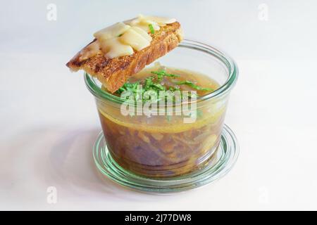 Zuppa di cipolla francese con erbe fresche verdi in un bicchiere e pane arrosto con formaggio fuso, sfondo grigio chiaro, spazio copia, fuoco selezionato, narro Foto Stock