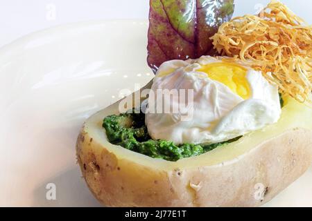 Patate farcite con spinaci, uova in camicia, paglia di sedano fritto e una foglia di erbe selvatiche, pasto sano su un piatto leggero, spazio copia, fuoco selezionato, stretto d Foto Stock