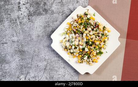 Insalata di bastoncini di granchio surimi con mais, cetriolo e alghe su un piatto quadrato bianco su sfondo scuro. Vista dall'alto, piatto Foto Stock