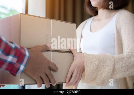 Primo piano addetto alla consegna in rosso uniforme che tiene il pacchetto mentre cliente donna firma su carta che riceve i documenti. Foto Stock