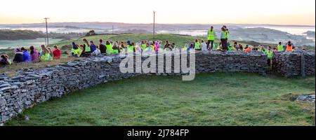 La folla che guarda l'alba sorgere del sole dopo l'oscurità nella luce cammina. Knockdrum pietra ring Fort, West Cork, Irlanda Foto Stock