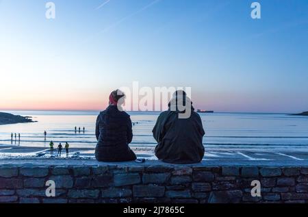 Fountainstown, Cork, Irlanda. 07th maggio 2022. Catherine Collins e John Corkish di Carrigaline si siedono su un muro e guardano i nuotatori che prendono parte al Darkness in Light Swim, che raccoglie fondi per Pieta House a Fountainstown, Co. Cork, Irlanda. - Credit; David Creedon / Alamy Live News Foto Stock