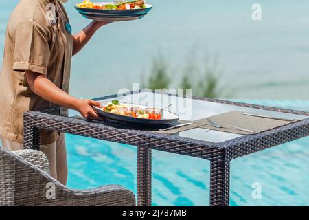 Una cameriera irriconoscibile ha messo i piatti sul tavolo nel ristorante all'aperto dell'hotel Foto Stock