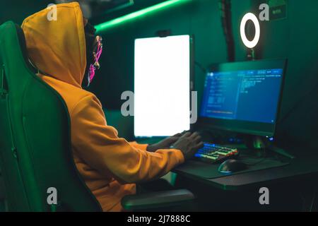 hacker in un cappuccio arancione e con una maschera hacking database mezzo sparato cyberterrorismo concetto indoor . Foto di alta qualità Foto Stock