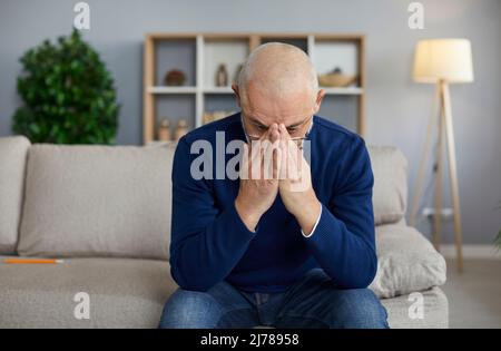 L'uomo anziano triste che sta addolorando per la perdita di sua moglie è seduto sul divano a casa Foto Stock