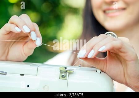 indiano cucito femminile all'aperto nel parco estivo primo piano messa a fuoco sulle mani filo l'occhio di un ago Foto Stock