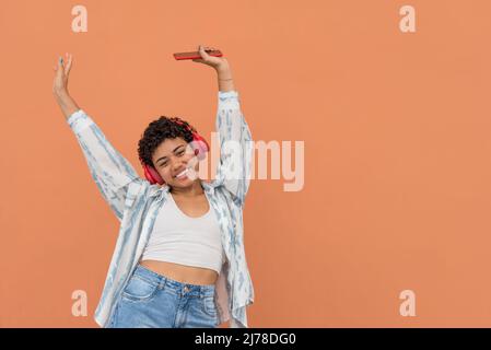 Ritratto di felice giovane donna latina con smartphone e auricolari che ballano per strada, Panama, America Centrale Foto Stock