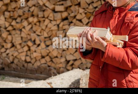 La bambina tiene la legna con la mano. Pila di legna da ardere accatastata preparata per riscaldare la casa. Raccolta legna da ardere per l'inverno o fuoco Foto Stock