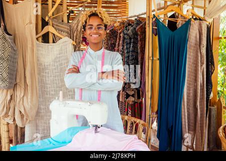 donna afroamericana in piedi e le braccia incrociate vicino alla sua macchina da cucire in laboratorio tropicale a Bali Foto Stock