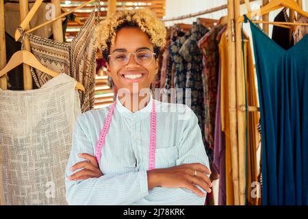 donna afroamericana in piedi e le braccia incrociate vicino alla sua macchina da cucire in laboratorio tropicale a Bali Foto Stock