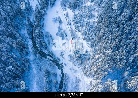 Strada nevosa con auto rossa che passa tra la foresta invernale. Vista aerea. Natura sfondo invernale. Foto Stock