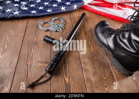 Manette, stivaletto nero e bastone da notte della polizia vicino alla bandiera degli Stati Uniti su superficie di legno Foto Stock