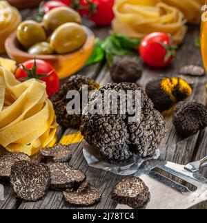 Tartufo invernale commestibile nero, tagliatelle e basilico fresco su tavola di legno. Gli ingredienti di cottura più popolari. Foto Stock