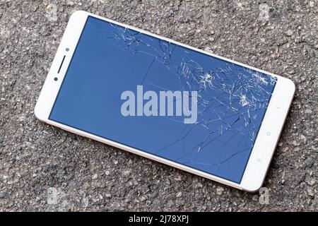 Lo smartphone con schermo blu rotto si trova sull'asfalto. Foto Stock