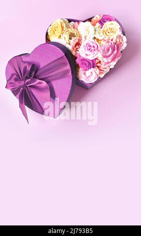Confezione regalo a forma di cuore e bouquet. Fiori un dono a forma di cuore. Rose in un cuore di scatola su sfondo rosa Foto Stock