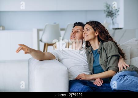 Sposi felici con capelli scuri sedersi su un comodo divano in soggiorno e discutere i piani per il futuro sorridendo ampiamente primo piano Foto Stock