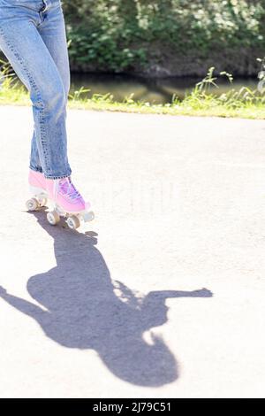 gambe donna in jeans e pattini rosa in un parco Foto Stock