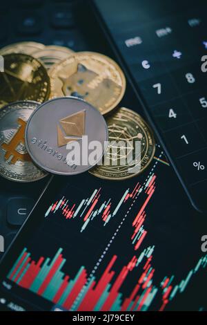 Stack o cumulo di oro varie criptovaluta vicino a un monitor con grafico a candela e calcolatrice digitale. Bitcoin, Ethereum, Cardano, Litecoin Foto Stock