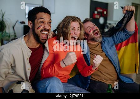Felici tifosi tedeschi amici che guardano il calcio a casa e festeggiano. Foto Stock