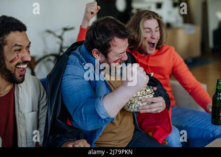 Felici tifosi tedeschi amici che guardano il calcio a casa e festeggiano Foto Stock