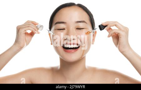 Donna che applica siero ialuronico sul viso con pipetta. Foto di donna asiatica con perfetto makeup sfondo bianco. Concetto di bellezza. Goccia essenziale Foto Stock