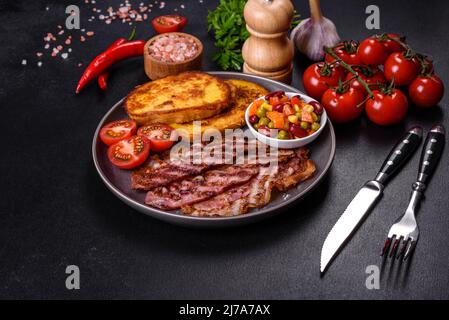 Fette di deliziosa pancetta alla griglia con crostini fritti in uovo con spezie, sale, verdure ed erbe su sfondo di cemento scuro Foto Stock