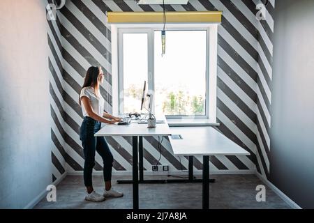 Posto di lavoro in piedi. Lavoro in posizione eretta. Scrivania in piedi per lavorare da casa o in ufficio. Giovane donna programmatore che lavora in piedi dentro Foto Stock