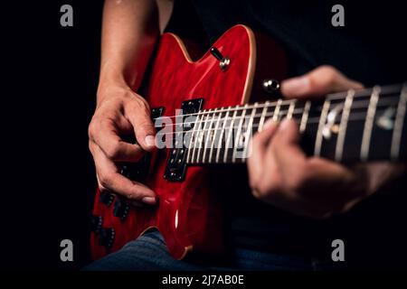 Primo piano di un uomo che suona una chitarra elettrica rossa lucida Foto Stock