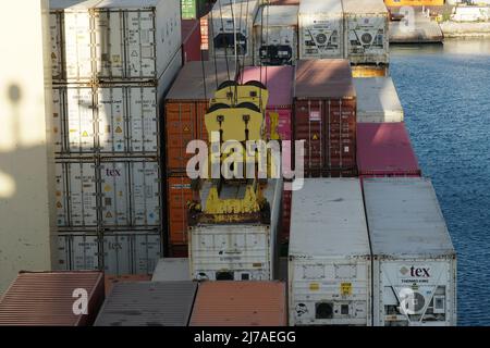 Vista ravvicinata del contenitore di carico fissato allo spanditore di gru a gantry azionate da stedores. Intorno sono stivati e schiacciati altri contenitori. Foto Stock