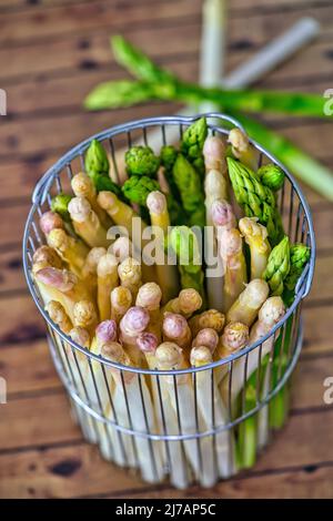 Nuova raccolta di asparagi bianchi e verdi tedeschi, mazzo di asparagi verdi e bianchi crudi in cesto con fondo di legno Foto Stock